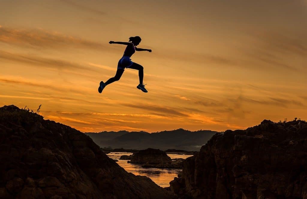 female athlete at dusk leaping over cliff